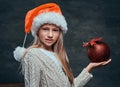 Teen boy wearing Santa`s hat holding a big Christmas ball on a dark textured background. Royalty Free Stock Photo