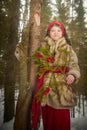 Portrait of Teen girl in thick coat, red sash and branch of fir tree with bright berries in cold winter day in forest