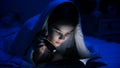 Closeup portrait of teen girl reading book under blanket Royalty Free Stock Photo