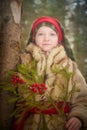 Portrait of Teen girl in thick coat, red sash and branch of fir tree with bright berries in cold winter day in forest