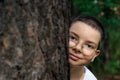 Portrait of a teenage boy with glasses peeking out from behind a tree Royalty Free Stock Photo