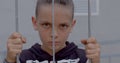 Portrait teenage boy hands holding on bars. He carefully looks in camera.