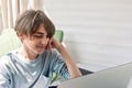 Portrait of teenage boy, sitting indoor and looking on laptop screen, lifestyle, bright natural sunlight. Royalty Free Stock Photo