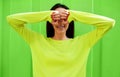 Portrait of teenage girl covering her eyes with both hands, wearing green long sleeves shirt. Outdoor image of smiling female has