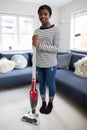 Portrait Of Teenage Girl Helping Out With Chores At Home Vacuuming Carpet In Lounge With Cordless Cleaner