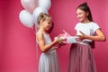 Portrait of a teenage girl on a pink background, with gifts, birthday concept, one gives another girl a gift