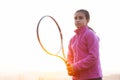 Portrait of teenage girl is training tennis skill outside court, in field at sunset. Wearing pink sweater and holding racket. Royalty Free Stock Photo