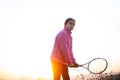 Portrait of teenage girl is training tennis skill outside court, in field at sunset. Wearing pink sweater. Royalty Free Stock Photo