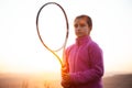 Portrait of teenage girl is training tennis skill outside court, in field at sunset. Wearing pink sweater. Royalty Free Stock Photo