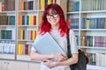 Portrait of teenage student female with backpack laptop looking at camera in college library Royalty Free Stock Photo