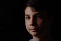 Portrait of a teenager on a black background. The boy has dark hair