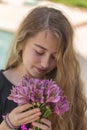 Portrait of a teenager girl with blonde hair smelling beautiful purple flowers