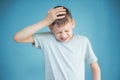 Portrait of a teenager in a gray t-shirt. Photo of a young boy on a blue background. He holds on to his head. The concept of Royalty Free Stock Photo