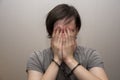 Portrait of a teenager in handcuffs covering his face with his hands on a gray background, medium plan. Juvenile delinquent, crimi