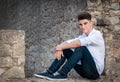 Portrait of a teenager. He is sitting in a stone wall. Dramatic