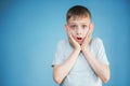 Portrait of a teenager in a gray t-shirt. Photo of a young boy looking at camera on a blue background. He is very surprised, his Royalty Free Stock Photo