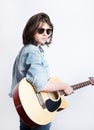 Side view portrait of a teenager wearing sunglasses and jeans jacket in studio background while holding a guitar Royalty Free Stock Photo