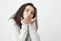 Portrait of tender lovely young female student sending kisses and showing it with gesture, over white background