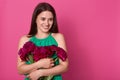 Portrait of tender positive young girl looking aside, keeping close bunch of flowers, enjoying bouquet of dark pink peonies, being