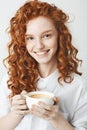 Portrait of tender redhead girl with freckles smiling holding cup looking at camera. White background. Royalty Free Stock Photo