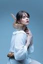 Portrait of tender young beautiful woman in white dress sitting with snake on her body, posing again blue-grey studio Royalty Free Stock Photo