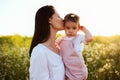 Portrait of tenderness of a pretty brunette mother kiss a daughter, toddler, baby, on sunset, flower field and nature background. Royalty Free Stock Photo