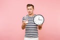 Portrait of tense caucasian man in striped t-shirt holding round clock, clear fresh pure water in glass isolated on