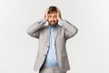 Portrait of tensed and distressed businessman with beard, wearing grey suit, holding hands on head and looking anxious Royalty Free Stock Photo