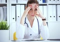 Portrait of tensed doctor sitting at the workplace in the hospital with hand on forehead in hospital