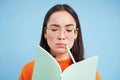 Portrait of thinking asian woman in glasses, solves task in notebook, writes down exercise, student learning, doing Royalty Free Stock Photo