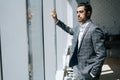 Portrait of thinking elegant business man wearing fashion suit standing in modern office room, looking out window. Royalty Free Stock Photo