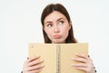 Portrait of thinking girl holding a notebook. Young woman with thoughtful face, holding weekly planner, checks her Royalty Free Stock Photo