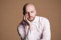 Portrait of thinking handsome bearded bald man in light pink shirt and white bow, sitting on chair touching his face with hand Royalty Free Stock Photo