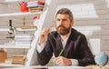 Portrait of thinking male teacher in school classroom. Teacher sitting on desk writing text in book at school classroom. Royalty Free Stock Photo