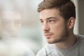 Portrait of thinking young man near glass window. Looking in the window. Reflection from model on the glass.