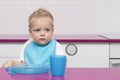 Portrait Of thoughtful adorable little kid in a blue bib In High Chair in the modern kitchen ready to eat. Copy space Royalty Free Stock Photo