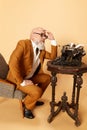 Portrait of thoughtful, bearded, mature, bald man in elegant, classical suit sitting near typewriter against studio