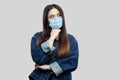 Portrait of thoughtful beautiful asian young woman with surgical medical mask in blue denim jacket standing, confused looking away
