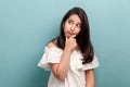 Portrait of thoughtful beautiful brunette young girl with black long straight hair in white dress standing, touching her chin, Royalty Free Stock Photo