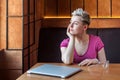 Portrait of thoughtful beautiful young bussineswoman with blonde short hair in pink t-shirt is sitting in cafe, finishing work and