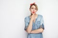 Portrait of thoughtful beautiful young woman in casual blue denim shirt with makeup and red headband standing touching her chin, Royalty Free Stock Photo