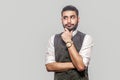 Portrait of thoughtful or confused handsome bearded brunette man in white shirt and waistcoat standing, holding his chin, looking Royalty Free Stock Photo