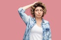 Portrait of thoughtful confused young woman with curly hairstyle in casual blue shirt standing scratching her head and thinking Royalty Free Stock Photo