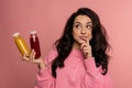 Pensive young brunette with a pair of bottled soft beverages posing for the camera on the pink background. Healthy drink Royalty Free Stock Photo