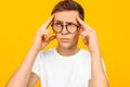 Portrait of a thoughtful dreamy guy with glasses and a white T-shirt, imagines something in mind, on a yellow background