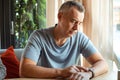 Portrait of thoughtful elderly man sitting at table on sofa near window, looking at watch, waiting for meeting. Date. Royalty Free Stock Photo