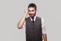 Portrait of thoughtful handsome bearded brunette man in white shirt, waistcoat standing scratching his head, looking at camera and Royalty Free Stock Photo