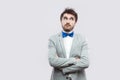 Portrait of thoughtful handsome bearded man in casual grey suit and blue bow tie standing with crossed arms, looking away and Royalty Free Stock Photo