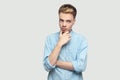 Portrait of thoughtful handsome young man in light blue shirt standing, holding his chin, thinking and looking away Royalty Free Stock Photo