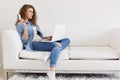 Portrait of thoughtful magnetic woman sitting with her laptop on sofa, holding credit card in one hand, thinking about purchases Royalty Free Stock Photo